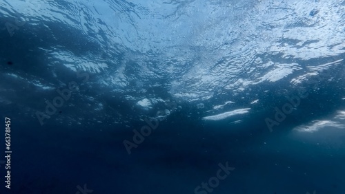 Sight from beneath the ocean floor as sunlight pierces through the water's surface. Watch as rising air bubbles twinkle and shimmer in the gentle illumination