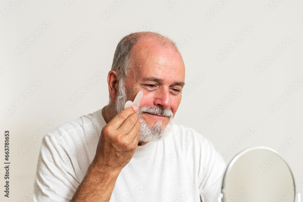 Elderly male massaging face while holding mirror Elderly male massaging face while holding mirror