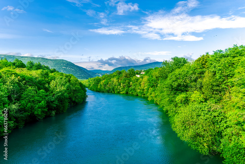 beautiful landscape of spring or summer sunset river with blue water and green hills on sides and mountains with amazing cloude sky on background
