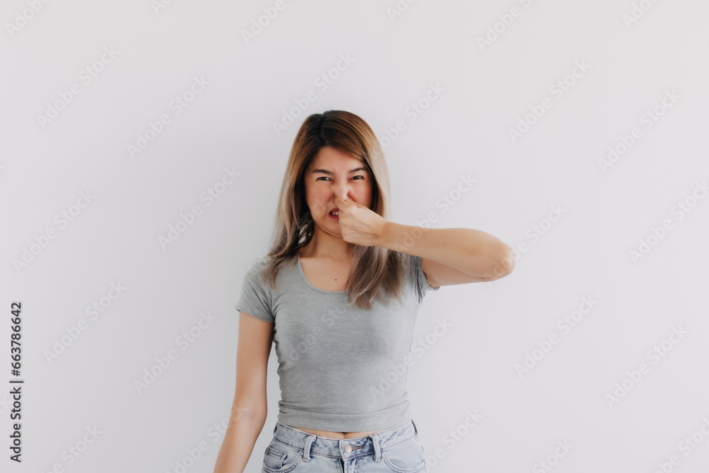 Unhappy Asian Thai woman wear grey, squeezing, pinching and holding nose, blocking bad smell, looking at camera smelly, isolated on white background wall. Unhappy Asian Thai woman wear grey, squeezing, pinching and holding nose, blocking bad smell, looking at camera smelly, isolated on white background wall.