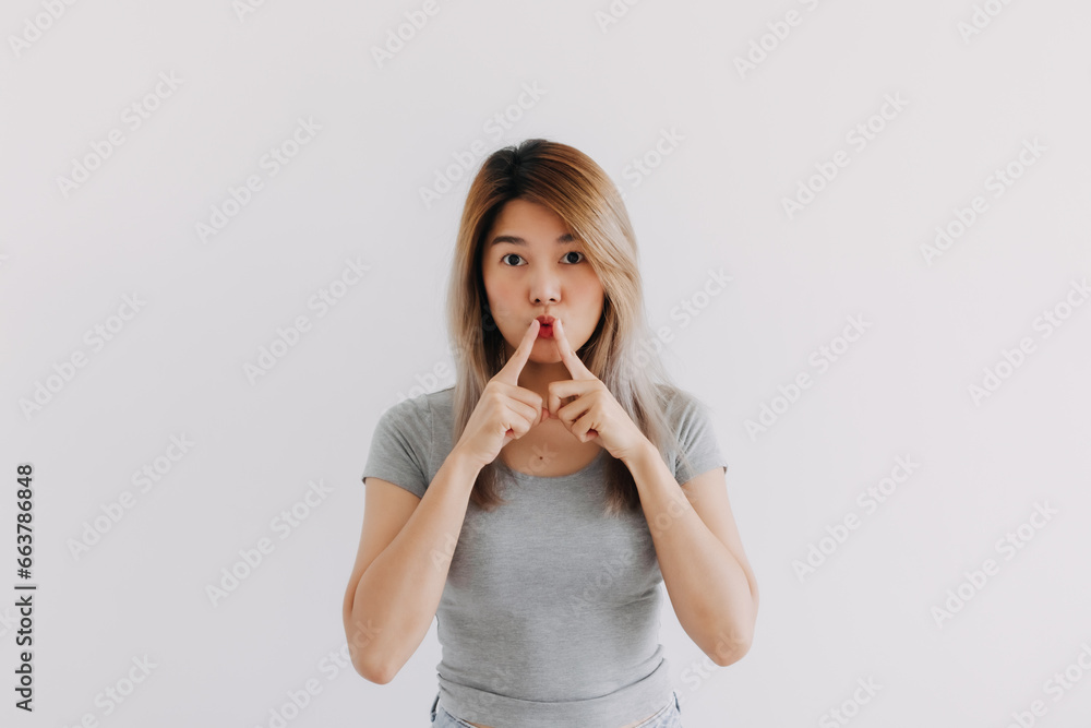 Asian Thai woman wear grey, touching mouth by both hands finger, showing quiet sign hush hand gesture, looking at camera isolated on white background wall. Asian Thai woman wear grey, touching mouth by both hands finger, showing quiet sign hush hand gesture, looking at camera isolated on white background wall.