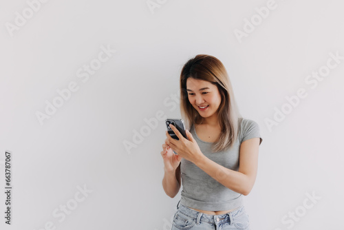 Asian Thai woman wear grey, happy smiling while using and looking at smartphone, texting and chatting with someone, isolated over white background.