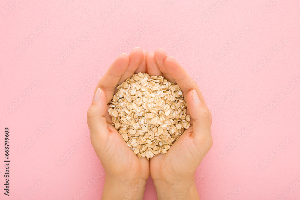 Young adult woman hands holding dry rolled oat on light pink table background. Pastel color. Closeup. Point of view shot. Healthy food. Top down view. - obrazy, fototapety, plakaty 
