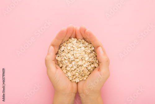 Young adult woman hands holding dry rolled oat on light pink table background. Pastel color. Closeup. Point of view shot. Healthy food. Top down view.