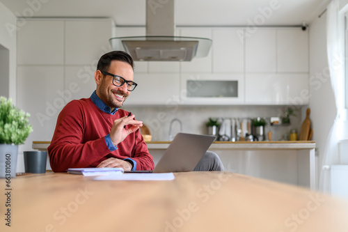 Smiling entrepreneur discussing over video call on laptop while sitting at desk in home office