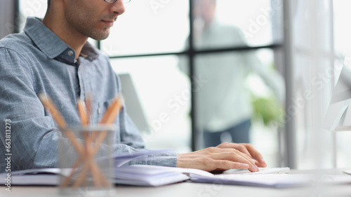 Side view of confident bearded concentrated businessman works on laptop while sitting at the table