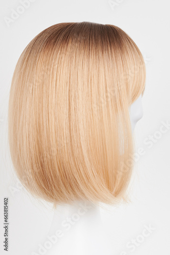 Natural looking blonde fair wig on white mannequin head. Short hair cut on the plastic wig holder isolated on white background  side view.