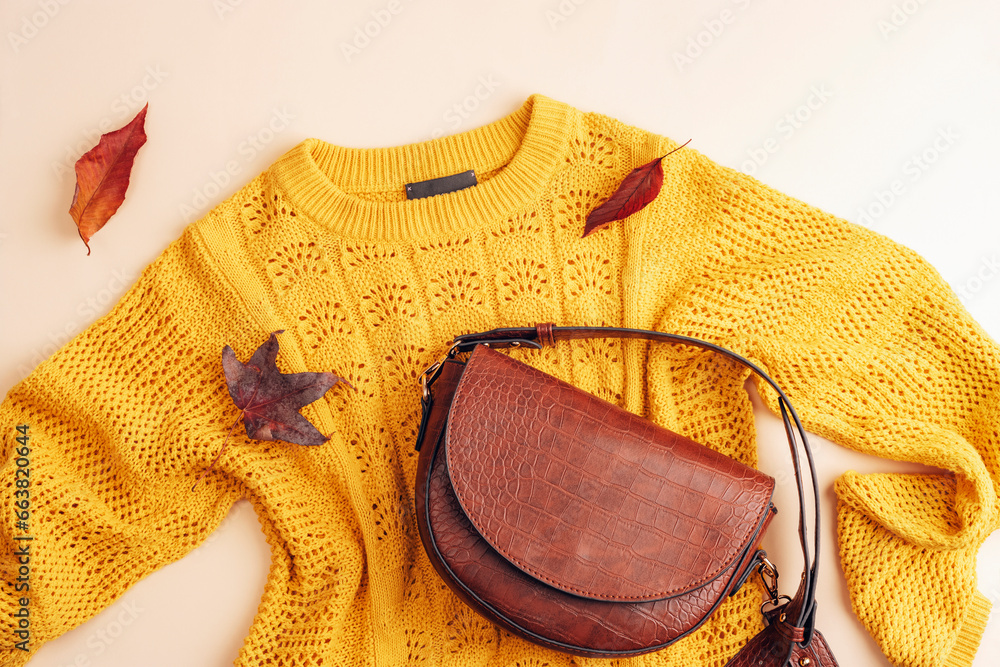 Φωτογραφία Flat lay of woman's yellow sweater and brown bag, autumn leaves on beige background