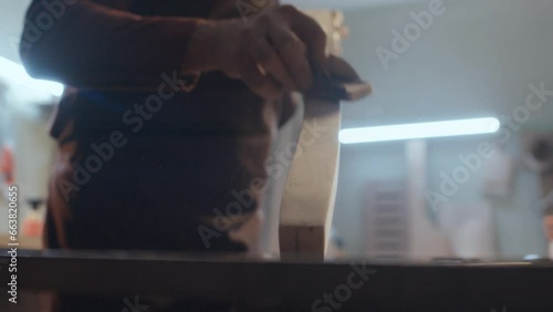 Selective focus close-up shot of unrecognizable male woodmaker using special technique on piece of timber while smoothing it out with sandpaper photo