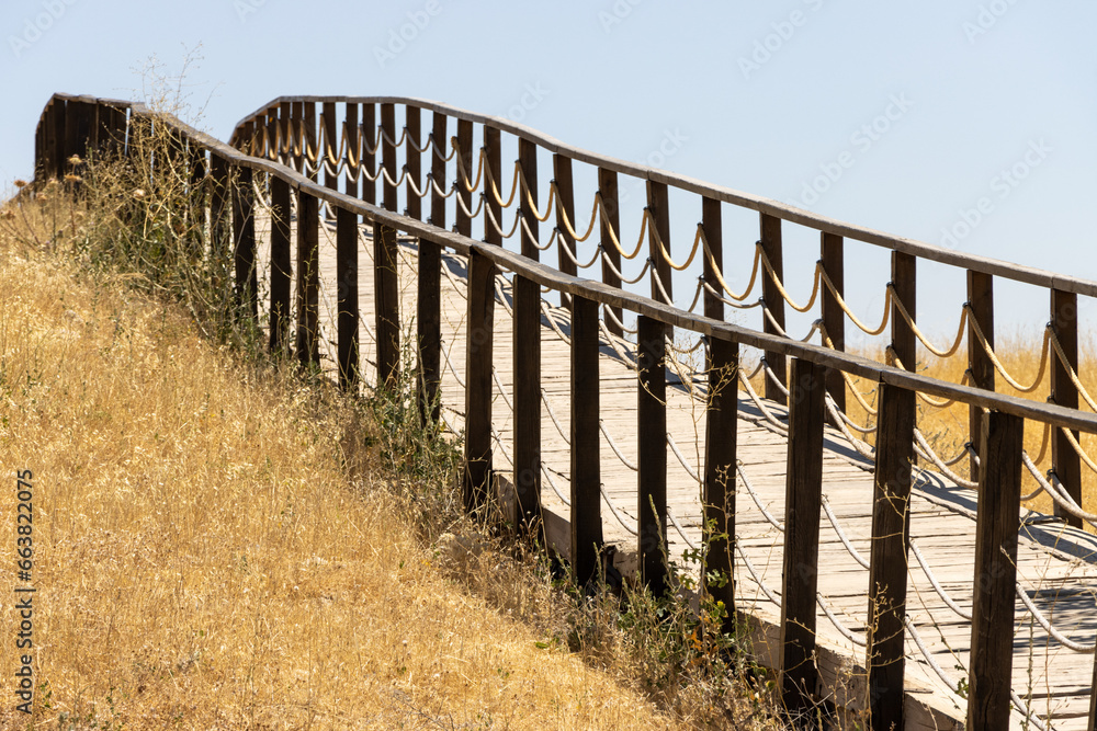 Naklejka premium Wooden fence bridge over meadow and grass. Made of rope ropes. Sidewalk pathway