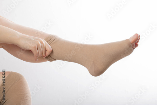 A woman puts on compression stockings for legs with varicose veins. Pain and swelling in the legs, phlebology. White background, close-up. Bloodstream