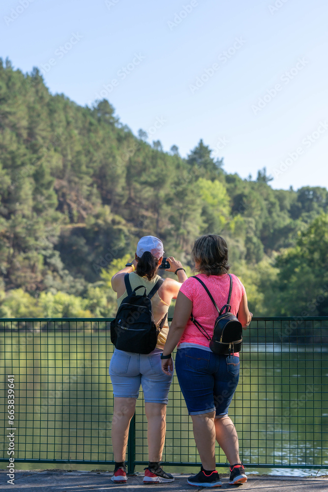 A couple of travelers with a backpack standing at the top of the nature viewpoint, enjoying the views on the surface of the Sil River, Spain, friends, sisters... etc. travel through nature in Galicia
