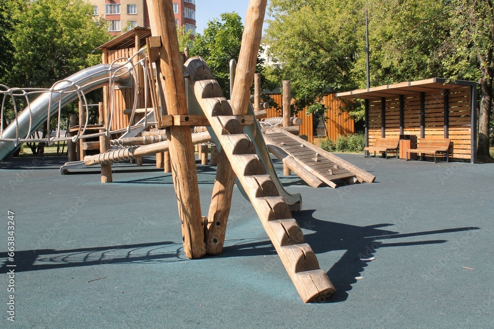 Wooden playground made of natural eco-friendly material in public city park. Modern safety children outdoor equipment. Concept of sustainable lifestyle and ecology. Children rest and games on open air - obrazy, fototapety, plakaty 