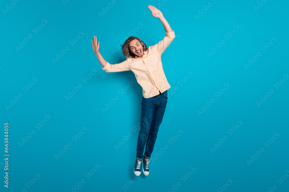 Full length photo of funny friendly positive guy wear stylish shirt denim trousers hold arms up fooling isolated on blue color background Full length photo of funny friendly positive guy wear stylish shirt denim trousers hold arms up fooling isolated on blue color background