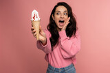 Woman screaming in horror at the sight of the vanilla ice cream waffle cone in her hand while standing in front of the camera on the pink background..