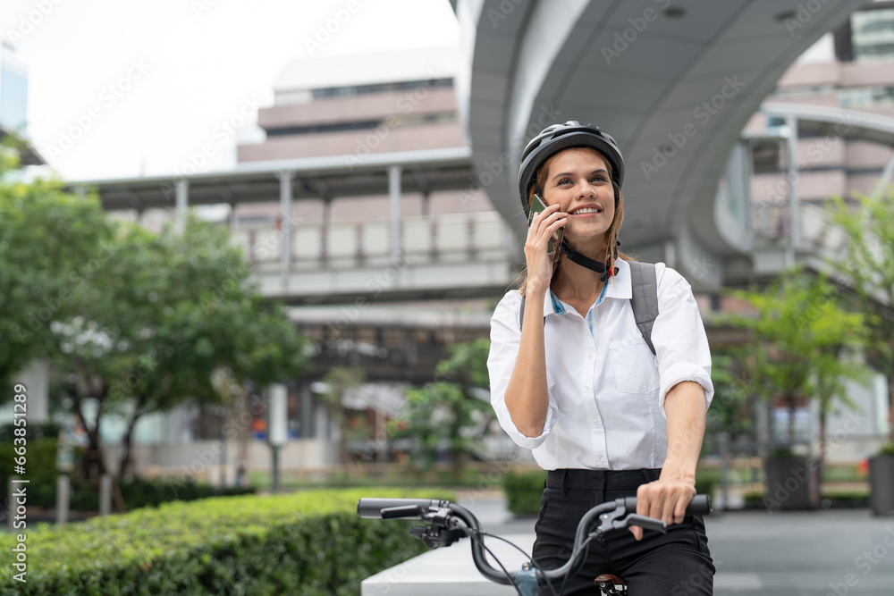 Businesswoman using smartphone while riding bicycle. Woman commuting on bike go to work in city. Eco friendly vehicle, sustainable lifestyle concept