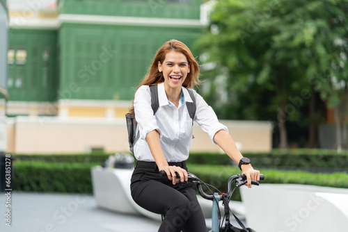 Businesswoman with helmet riding bicycle on road go to work at office. Happy woman commuting on bike in city. Eco friendly vehicle, sustainable lifestyle concept.
