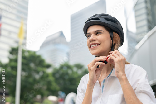 Businesswoman putting cycling helmet prepared go to work at office. Close up female smile and wearing helmet safety ride bicycle on street in city. eco-friendly vehicle, sustainable lifestyle concept photo