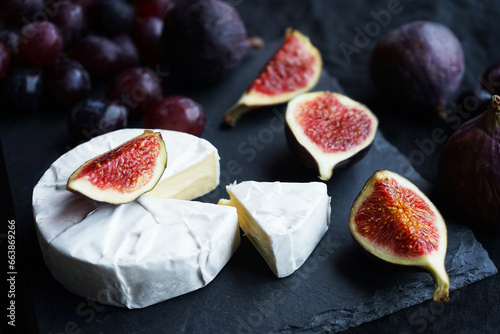 Ripe figs, red grapes with Camembert cheese next to cutlery on a dark background