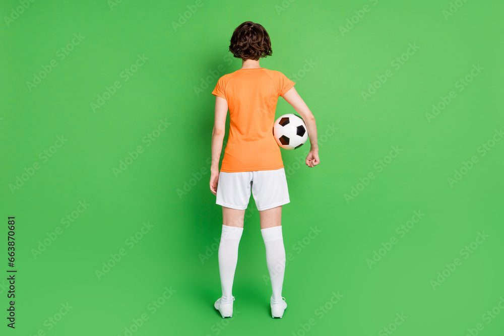 Full size rear portrait of young girl standing arm holding football isolated on green color background