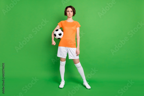 Fototapeta Naklejka Na Ścianę i Meble -  Full size photo of focused young girl standing hand hold football look camera isolated on green color background