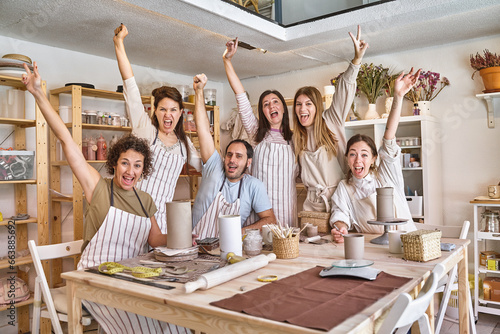 Group of creative people in aprons posing together while having fun in a pottery class. Hobby and craft concept.