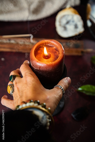 hand of a woman with jewels holding a lighted candle during a fortune telling session