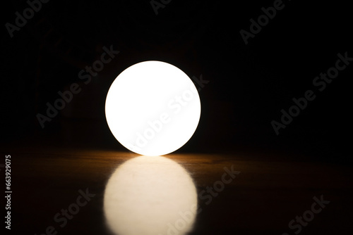 A round light ball on a wooden table with a dark background.