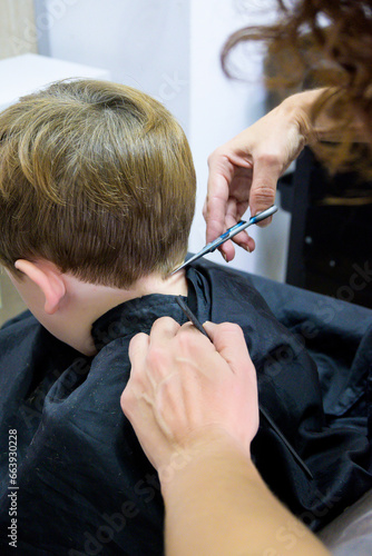 A little cute boy sits in a hairdresser's at the stylist's, a schoolchild is getting hair cut in a beauty salon, a child at a barbershop's, a short men's haircut