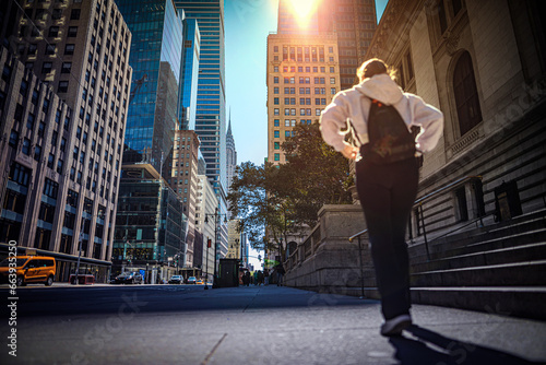 Canvas Print A girl walking on the sidewalk, illuminated by the rays of the sun piercing through the tall buildings of New York City