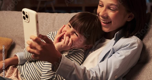 Brother and sister share a moment of pure joy, laughing heartily as they enjoy the content on phone together. Their faces light up with happiness, and the room echoes with contagious laughter.
