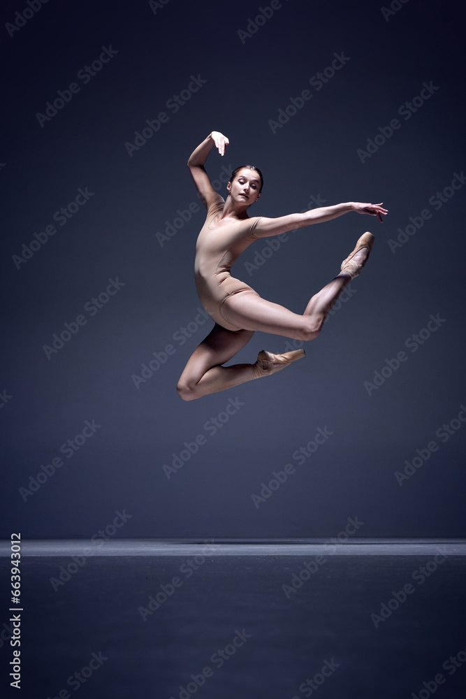 Elegance in movement. Tender young woman, ballerina in beige bodysuit dancing against blue studio background. Concept of classical dance, art and grace, beauty, choreography, inspiration