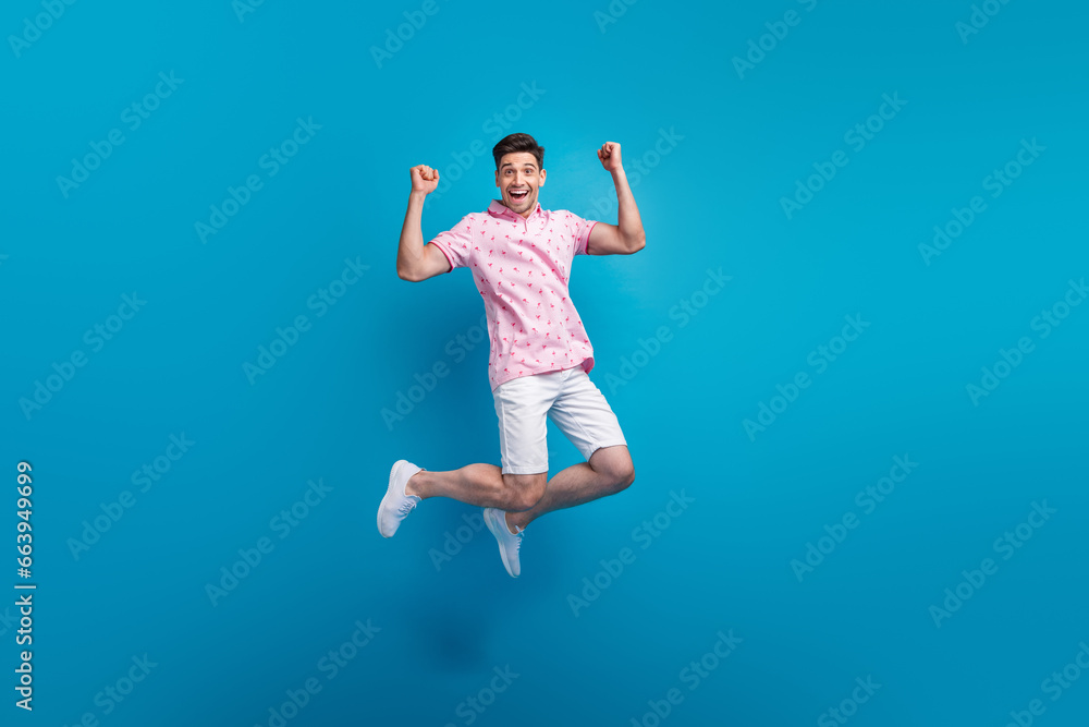 Full body portrait of crazy energetic young man jumping raise fists accomplishment isolated on blue color background