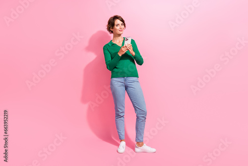 Full body length photo of charming girl influencer using smartphone to repost social media content isolated on pink color background