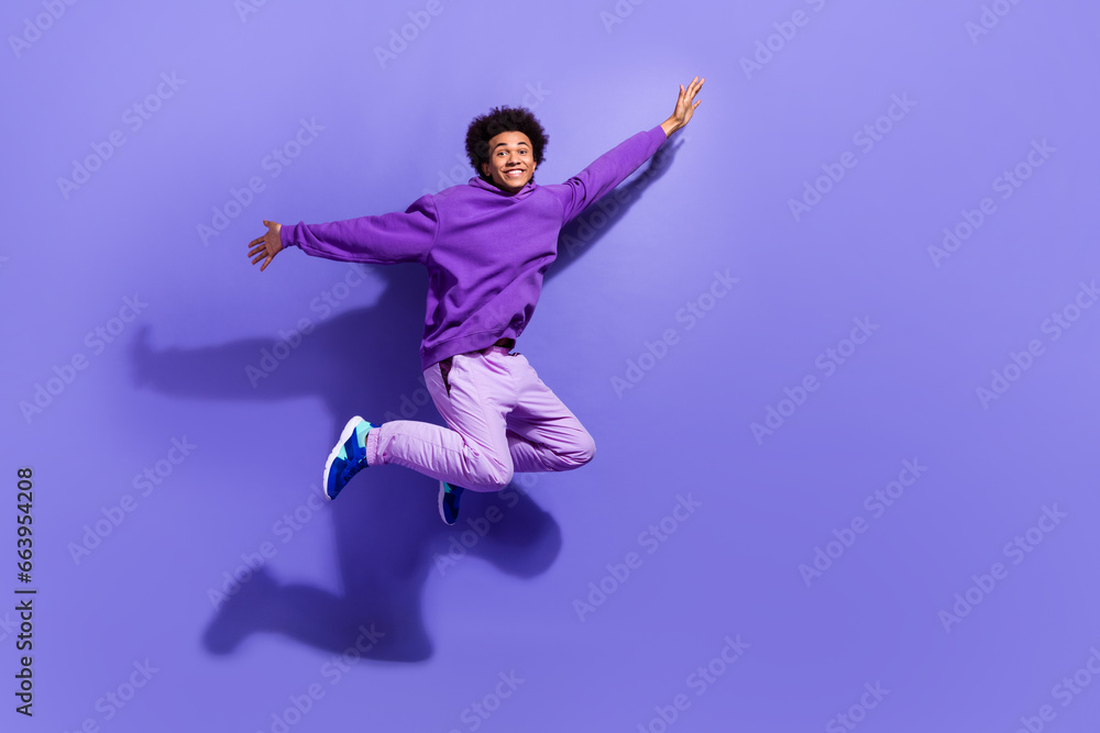 Full length photo of satisfied guy wear purple sportswear pullover flying hold arms like wings isolated on violet color background Full length photo of satisfied guy wear purple sportswear pullover flying hold arms like wings isolated on violet color background