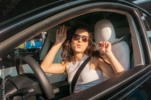 Happy pretty lady in sunglasses driving car on the road on sunny day while dancing the music. Travel adventure drive, happy summer vacation concept © Nataliya