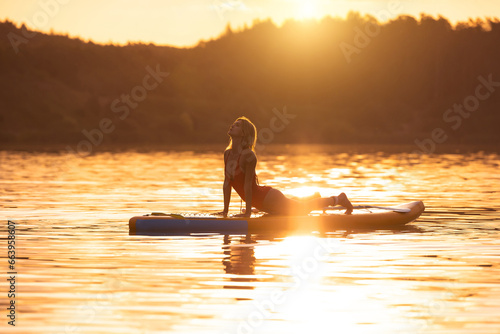 Beautiful woman practicing yoga on paddle sup surfboard. © zinkevych