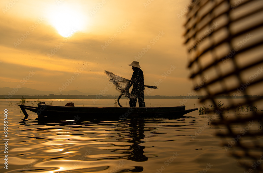 Silhouette of fisherman at sunrise, Standing aboard a rowing boat and casting a net to catch fish for food