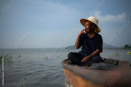 A fisherman relaxes in a boat on the lake while smoking. © Wosunan