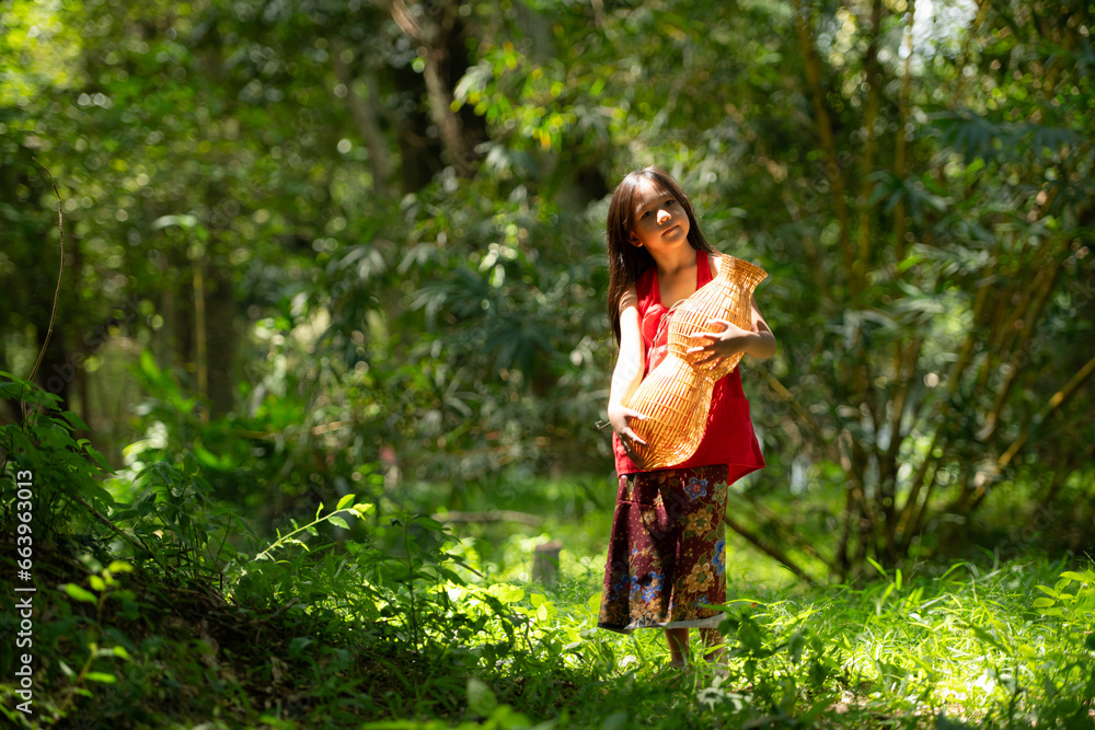 Little asian girl in red dress holding fishing equipment in the forest, Rural Thailand living life concept