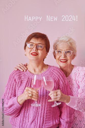 Two mature women in pink sweaters, drinking wine and celebrating 