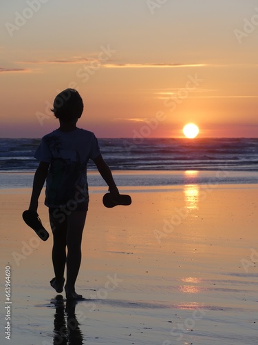 garçon serein marchant sur la plage en direction du soleil couchant 