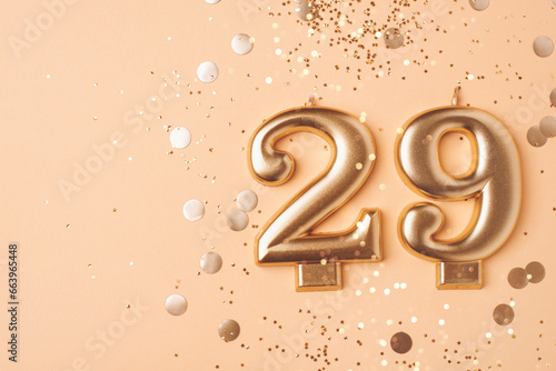 29 years celebration. Greeting banner. Gold candles in the form of number twenty nine on peach background with confetti. photo