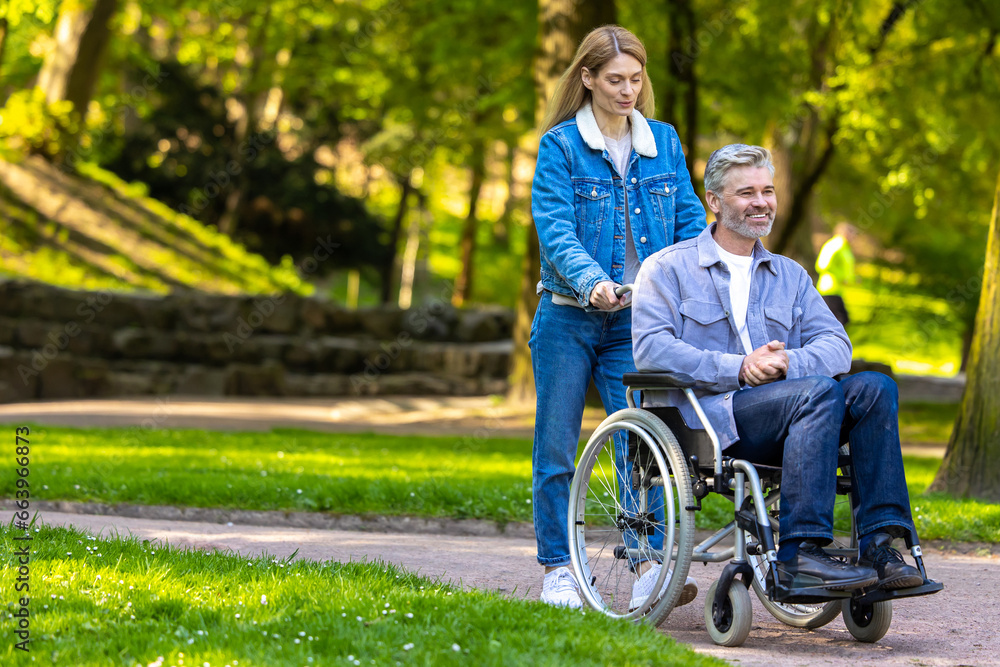 Woman rolling a wheelchair with her husband in the park and both looking happy Woman rolling a wheelchair with her husband in the park and both looking happy