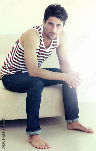 Serious, portrait and man on sofa for fashion in home, living room or house. Confidence, style and person on couch in lounge in trendy jeans, casual clothes and sitting to relax in apartment in Spain © M Moller/peopleimages.com
