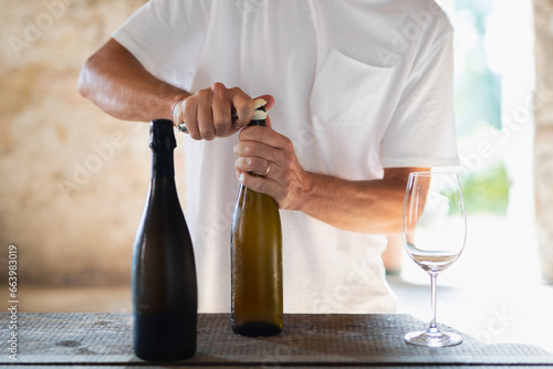 Un ragazzo con maglietta bianca stappa il vino. DUe bottiglie di vino senza etichetta perfette per mockup in ambiente luminoso.