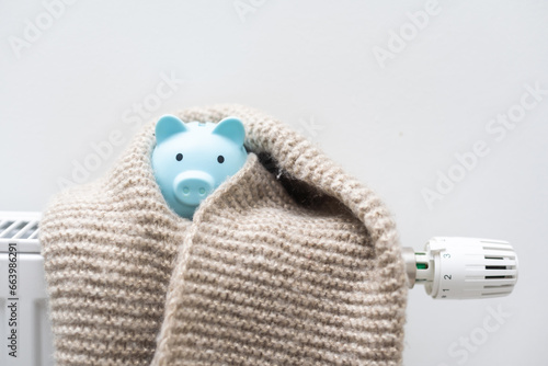 Piggy bank with scarf on radiator. Concept of heating season.