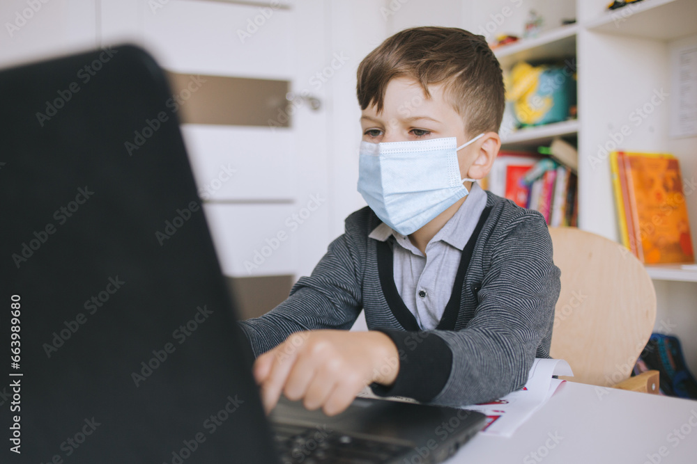 A child wearing a mask studies at home. A young student wearing a surgical mask does homework on the computer. Homeschooling During Viruses, Flu, and Seasonal Pandemics A child wearing a mask studies at home. A young student wearing a surgical mask does homework on the computer. Homeschooling During Viruses, Flu, and Seasonal Pandemics