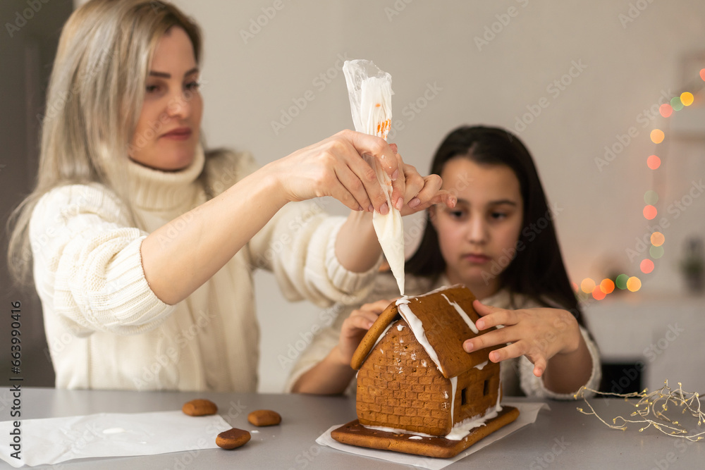 Mother and daughter making gingerbread cookies house, decorating at home, Christmas concept Mother and daughter making gingerbread cookies house, decorating at home, Christmas concept