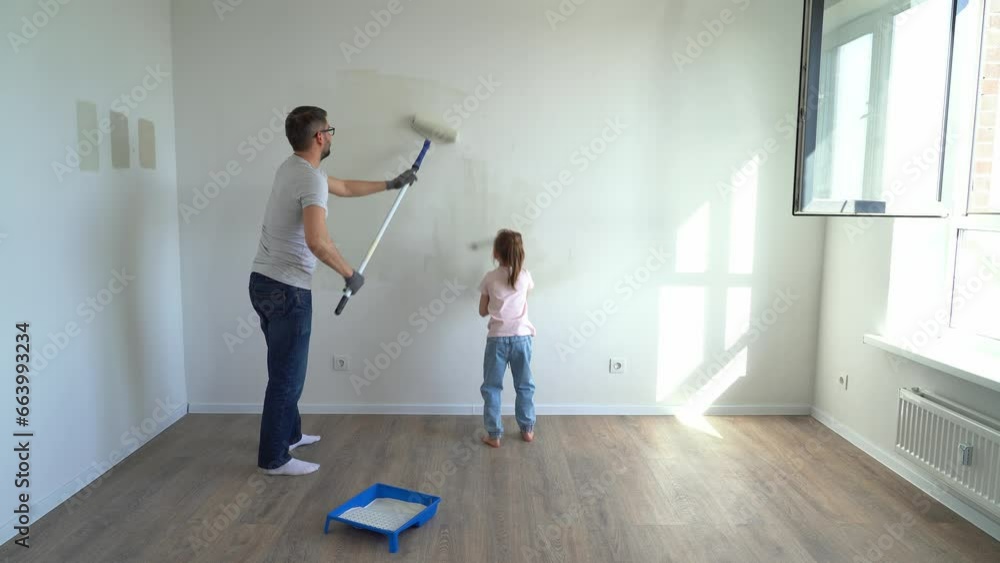Back view father and little daughter paint wall with rollers at home in ...